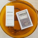 Sangle de transport dans sa boite de rangement et spray parfumé dans sa boîte de la marque Hercule Studio photo lifestyle sur table