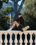 Tapis de sport couleur Pistache de la marque Hercule Studio avec sangle de transport Soca en cuir végétal photo lifestyle avec mannequin sur balcon