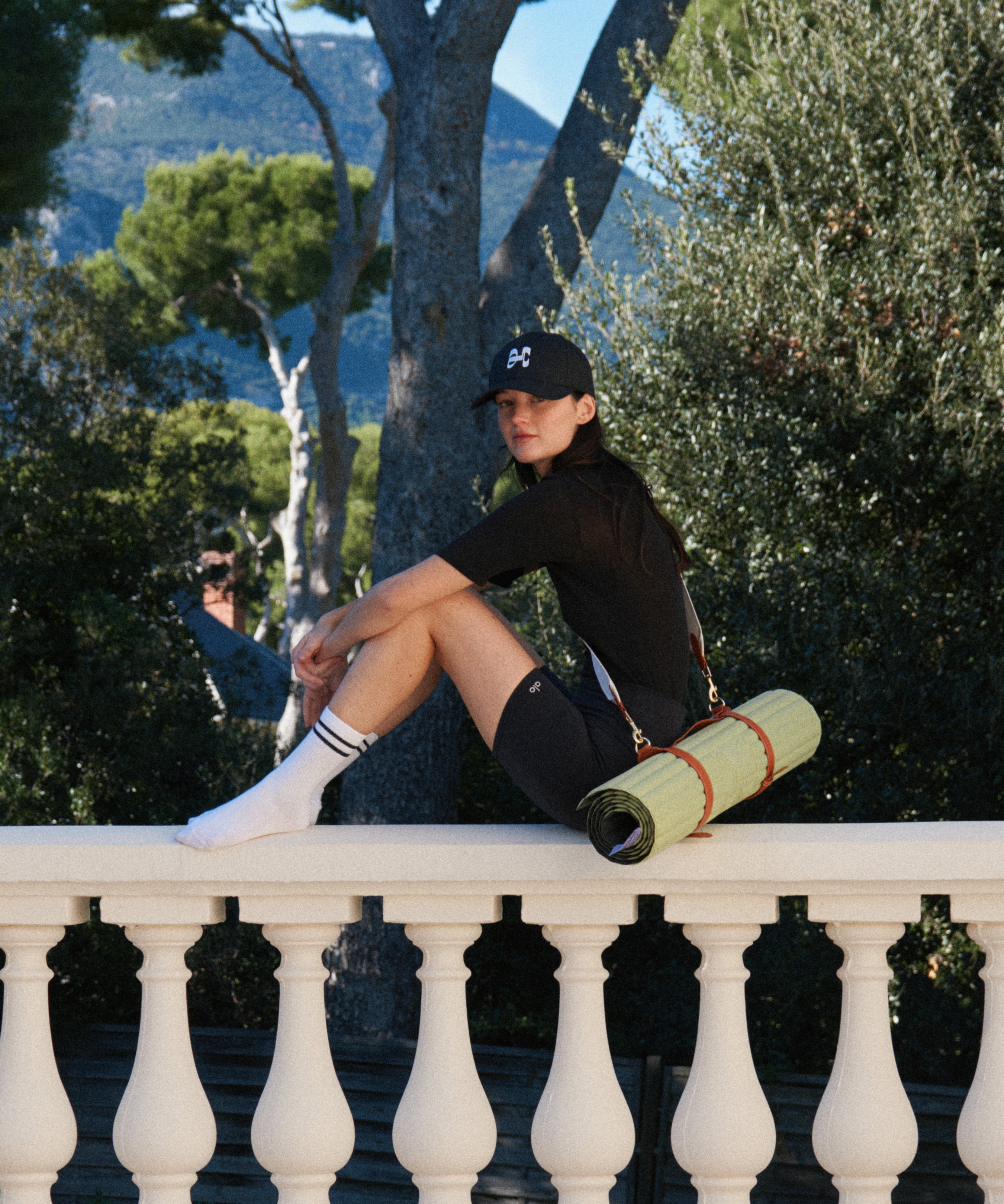 Tapis de sport couleur Pistache de la marque Hercule Studio avec sangle de transport Soca en cuir végétal photo lifestyle avec mannequin sur balcon