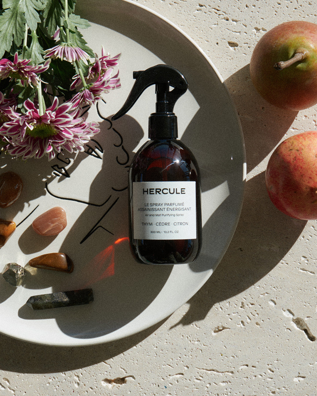 Spray pour assainir le tapis de sport et énergiser l'espace d'entraînement photo du produit sur une assiette et disposition de fleurs et pierres 