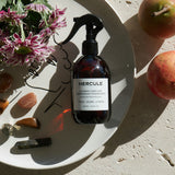 Spray pour assainir le tapis de sport et énergiser l'espace d'entraînement photo du produit sur une assiette et disposition de fleurs et pierres 