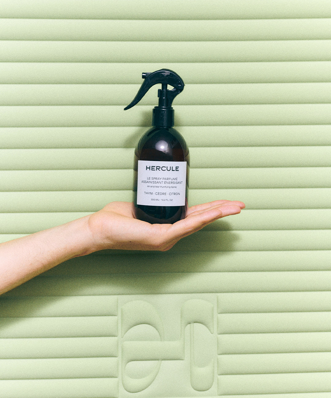 Spray pour assainir le tapis de sport et énergiser l'espace d'entraînement photo du produit devant le tapis archy pistache tenu dans la main