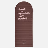 Hercule Studio x Thomas Lélu Limited Edition Exercise Mat, brown designer floor mat featuring a pink quote reading “focus on improving not proving,” an artistic collaboration for fitness, Pilates, and stretching, unfolded view
